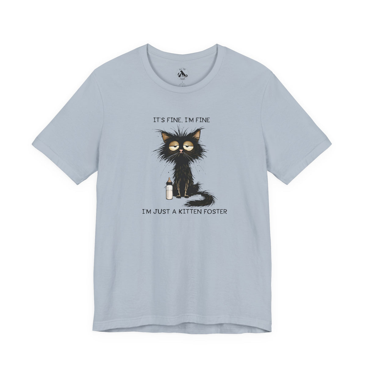 A light blue crewneck t-shirt featuring a cartoon graphic of a black cat with messy hair holding a bottle, with the text 'IT'S FINE. I'M FINE' above and 'I'M JUST A KITTEN FOSTER' below.